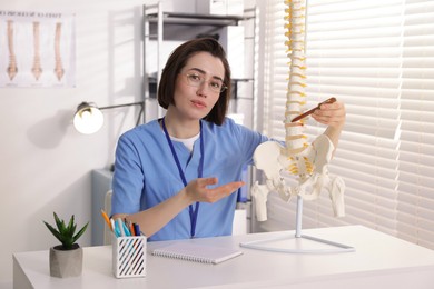 Photo of Doctor pointing at sections of human spine model at desk in clinic