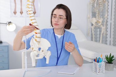 Photo of Doctor pointing at sections of human spine model at desk in clinic