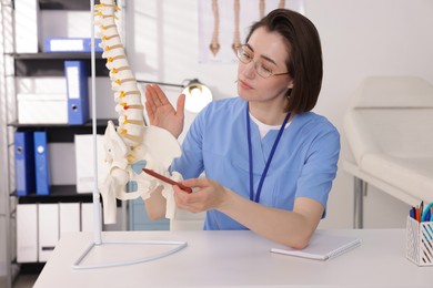 Photo of Doctor pointing at sections of human spine model at desk in clinic