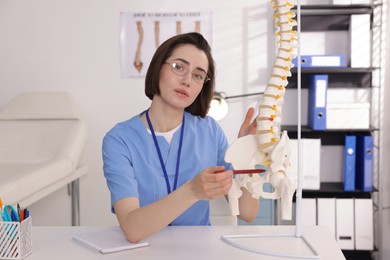 Photo of Doctor pointing at sections of human spine model at desk in clinic