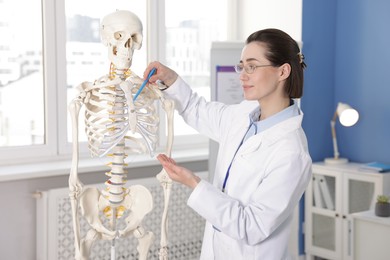 Photo of Doctor pointing at sections of human skeleton model in clinic