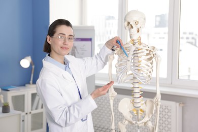Photo of Doctor pointing at sections of human skeleton model in clinic