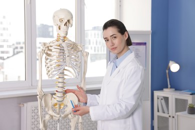 Photo of Doctor pointing at sections of human skeleton model in clinic