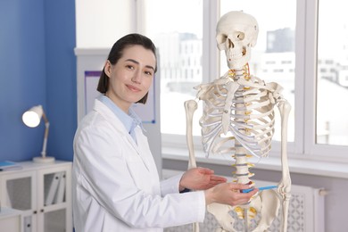 Photo of Doctor pointing at sections of human skeleton model in clinic