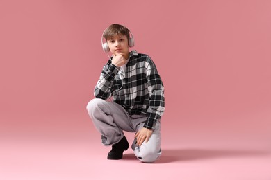 Photo of Boy with headphones in stylish clothes dancing on pink background