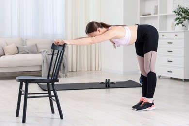 Photo of Young woman exercising with chair at home