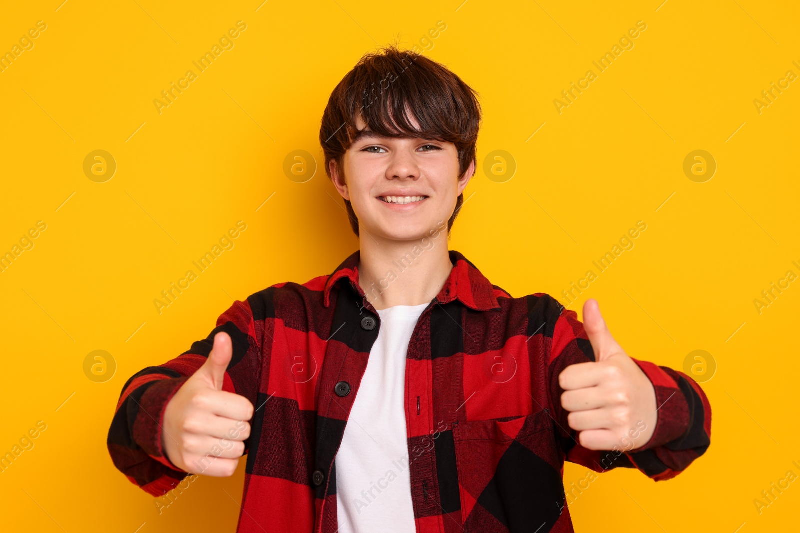 Teenage boy showing thumbs up on orange background Photo of Teenage boy showing thumbs up on orange background