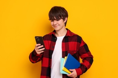 Photo of Teenage boy with smartphone and notebooks on orange background