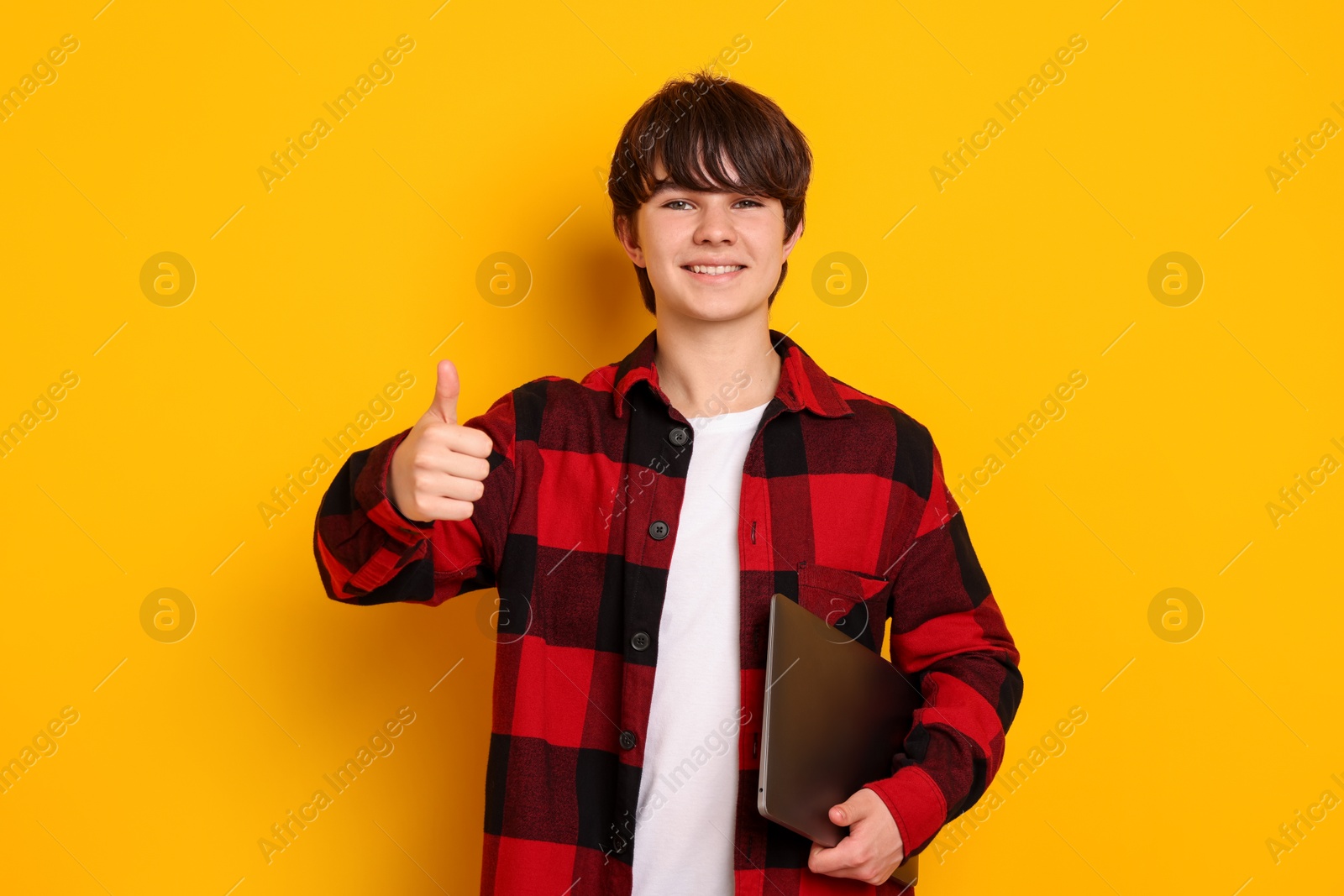Teenage boy with laptop showing thumbs up on orange background Photo of Teenage boy with laptop showing thumbs up on orange background