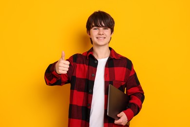Photo of Teenage boy with laptop showing thumbs up on orange background