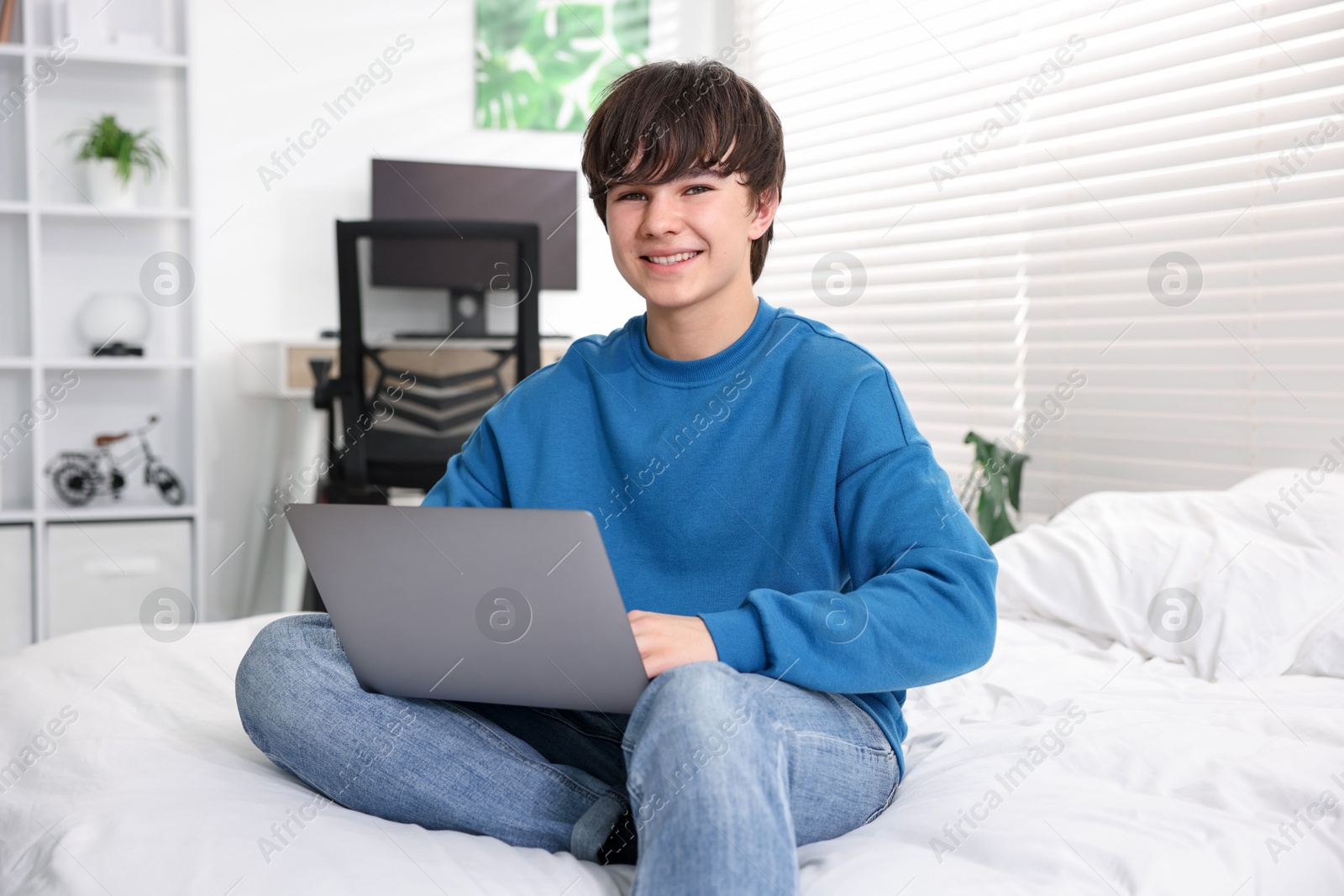 Teenage boy with laptop on bed at home Photo of Teenage boy with laptop on bed at home