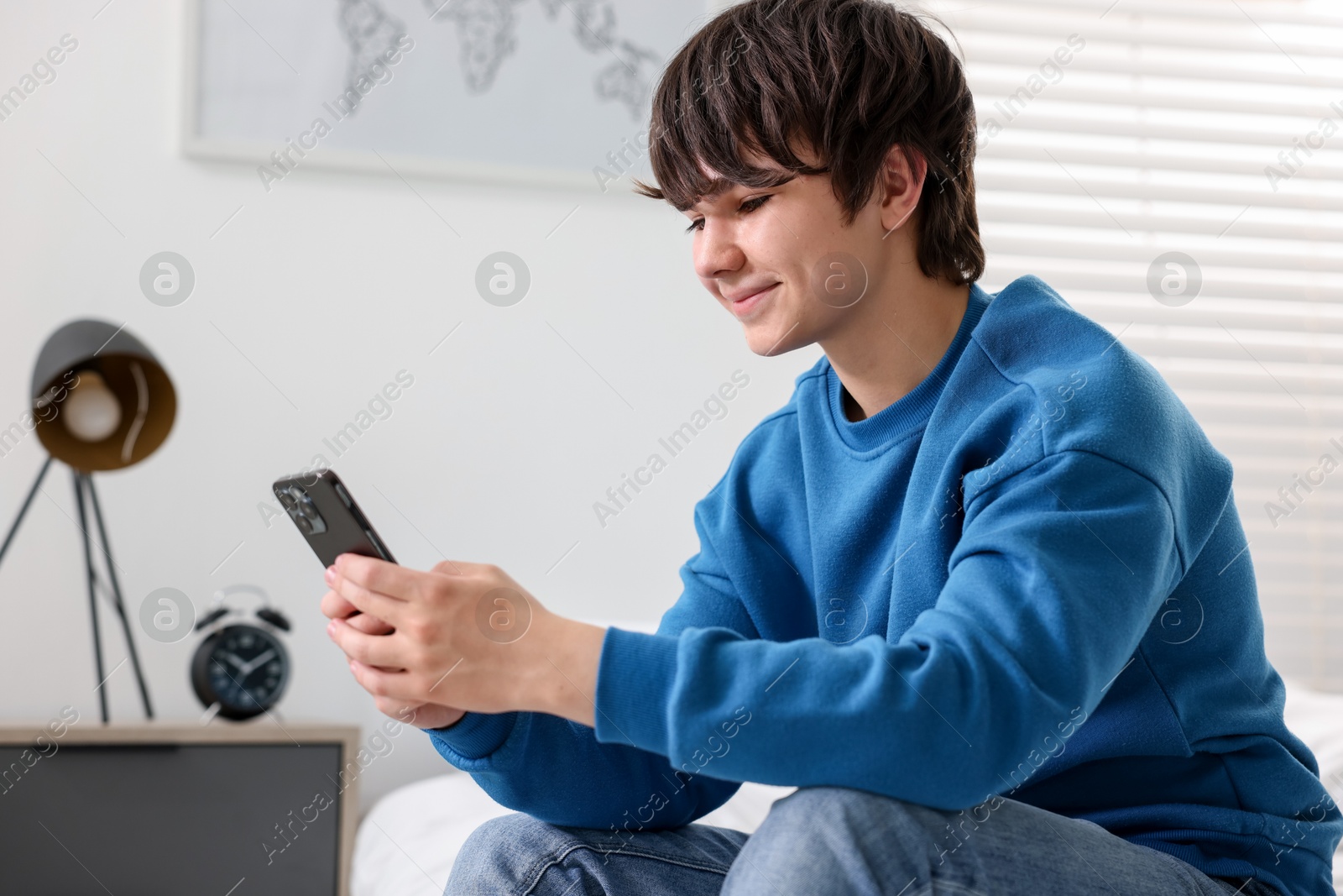 Teenage boy with smartphone on bed at home Photo of Teenage boy with smartphone on bed at home