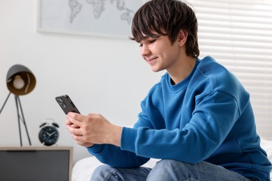 Photo of Teenage boy with smartphone on bed at home