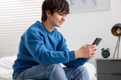 Photo of Teenage boy with smartphone on bed at home