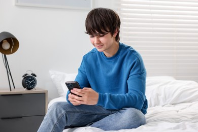Photo of Teenage boy with smartphone on bed at home