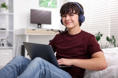 Photo of Teenage boy in headphones using laptop at home