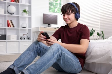 Photo of Teenage boy in headphones using smartphone at home