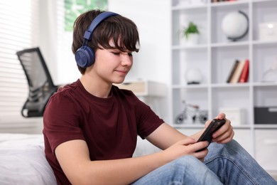 Photo of Teenage boy in headphones using smartphone at home
