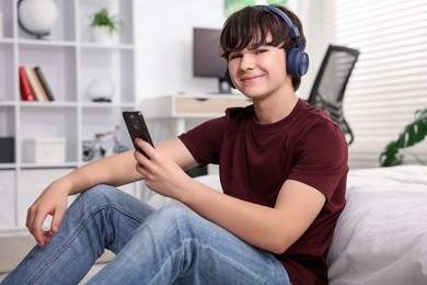 Photo of Teenage boy in headphones using smartphone at home