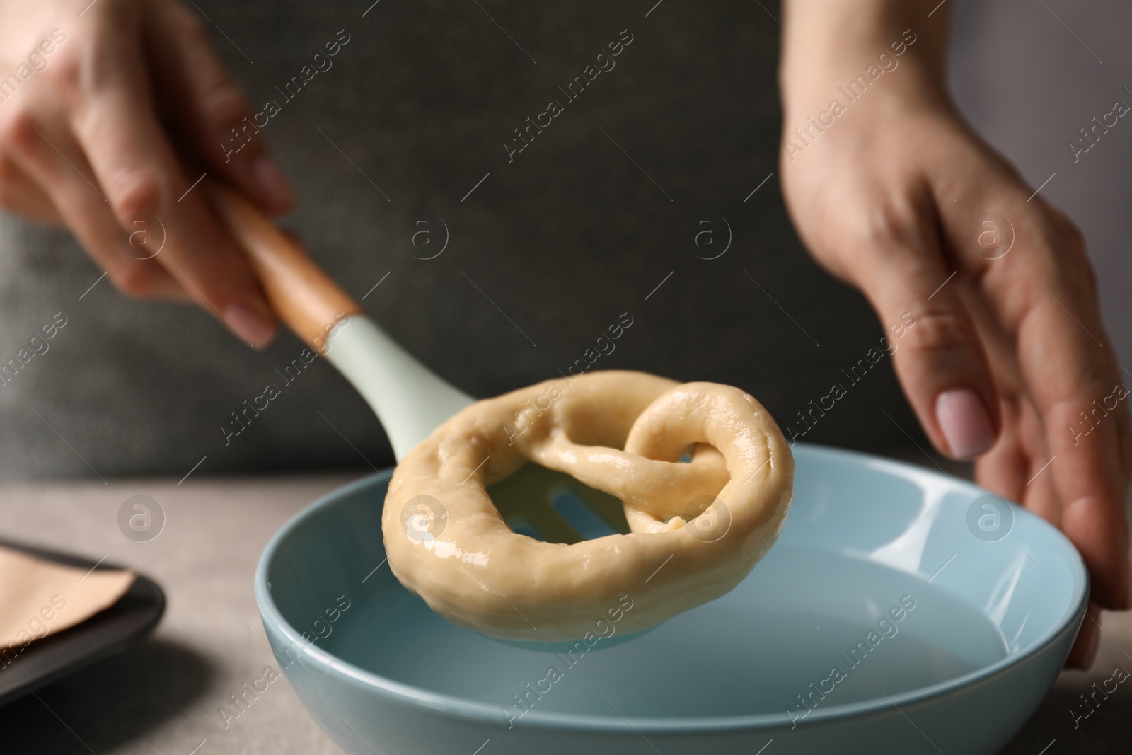 Woman putting uncooked pretzel into bowl of water at table, closeup Photo of Woman putting uncooked pretzel into bowl of water at table, closeup