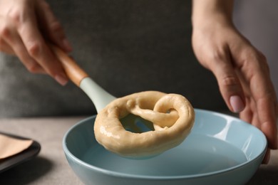 Photo of Woman putting uncooked pretzel into bowl of water at table, closeup