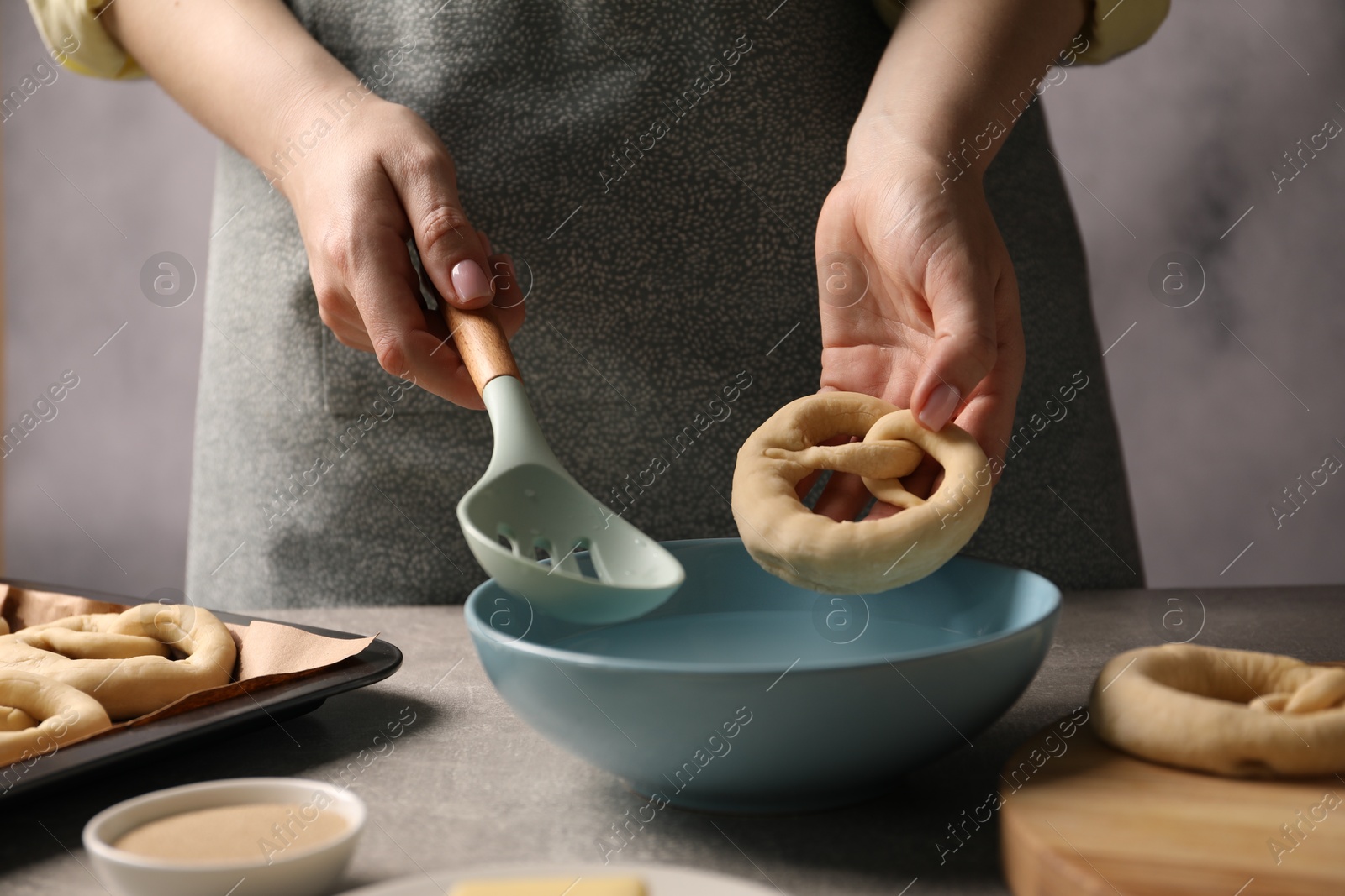 Woman putting uncooked pretzel into bowl of water at grey table, closeup Photo of Woman putting uncooked pretzel into bowl of water at grey table, closeup