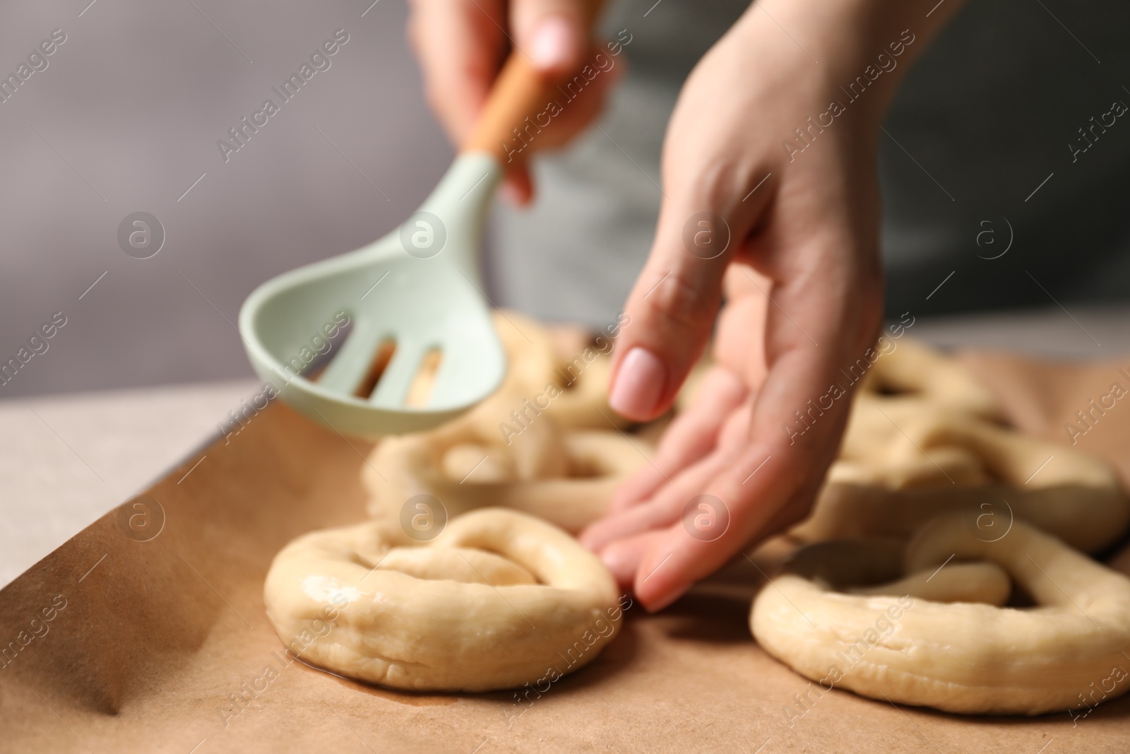 Woman putting uncooked pretzel onto baking dish at table, closeup Photo of Woman putting uncooked pretzel onto baking dish at table, closeup