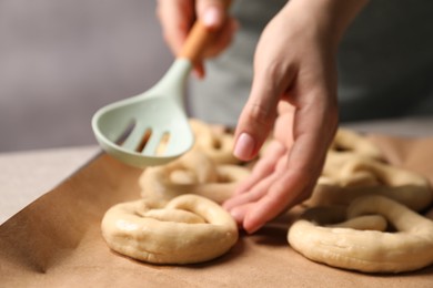 Photo of Woman putting uncooked pretzel onto baking dish at table, closeup