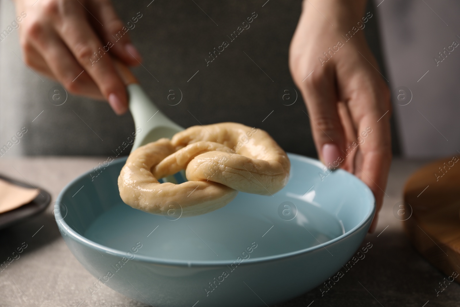 Woman putting uncooked pretzel into bowl of water at table, closeup Photo of Woman putting uncooked pretzel into bowl of water at table, closeup