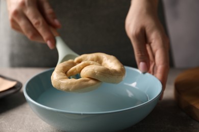 Photo of Woman putting uncooked pretzel into bowl of water at table, closeup