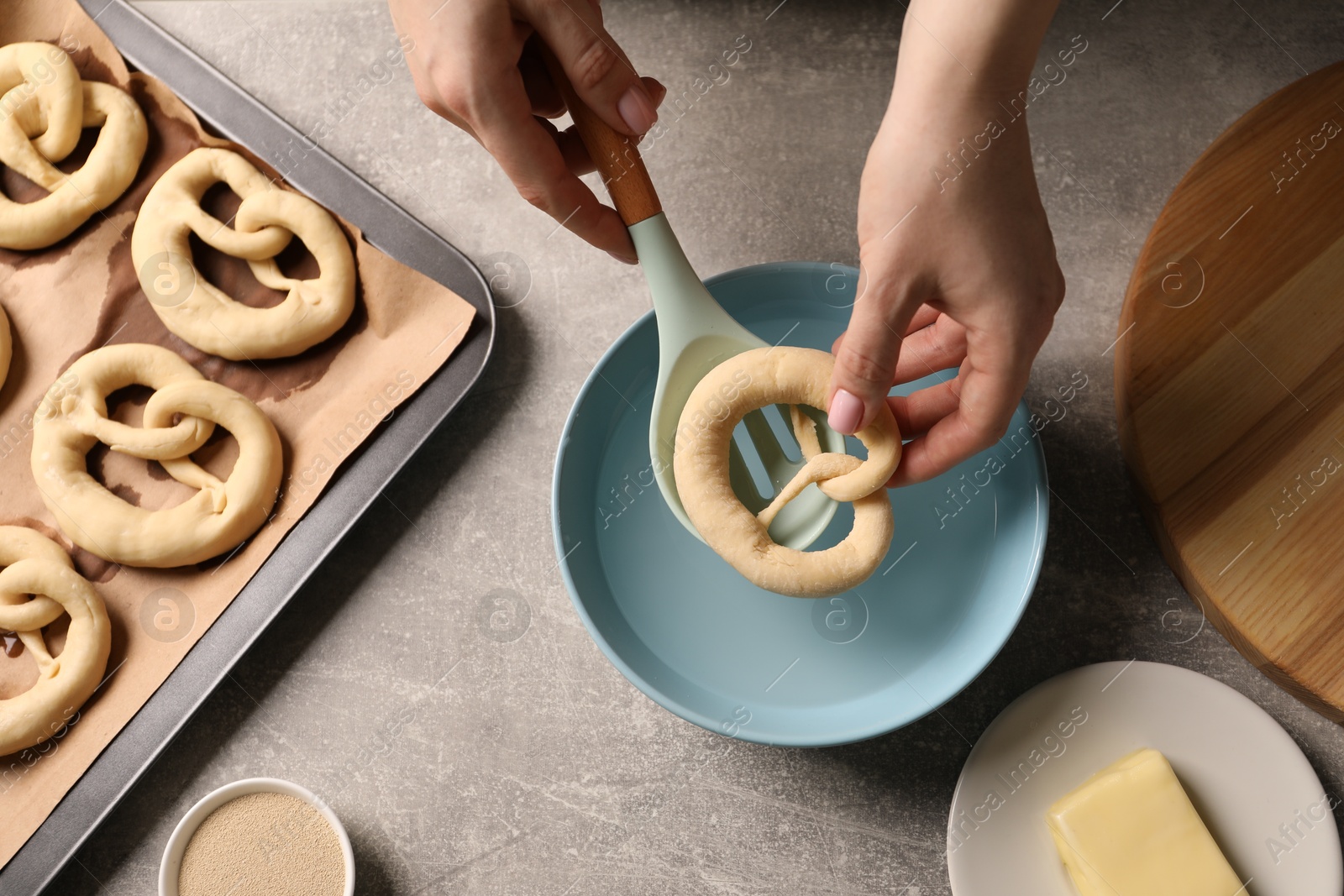 Woman putting uncooked pretzel into bowl of water at grey table, top view Photo of Woman putting uncooked pretzel into bowl of water at grey table, top view