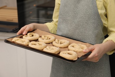 Photo of Woman holding baking dish with uncooked pretzels in kitchen, closeup