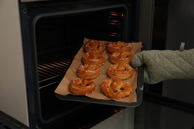 Photo of Woman taking baking dish with fresh pretzels out of oven, closeup