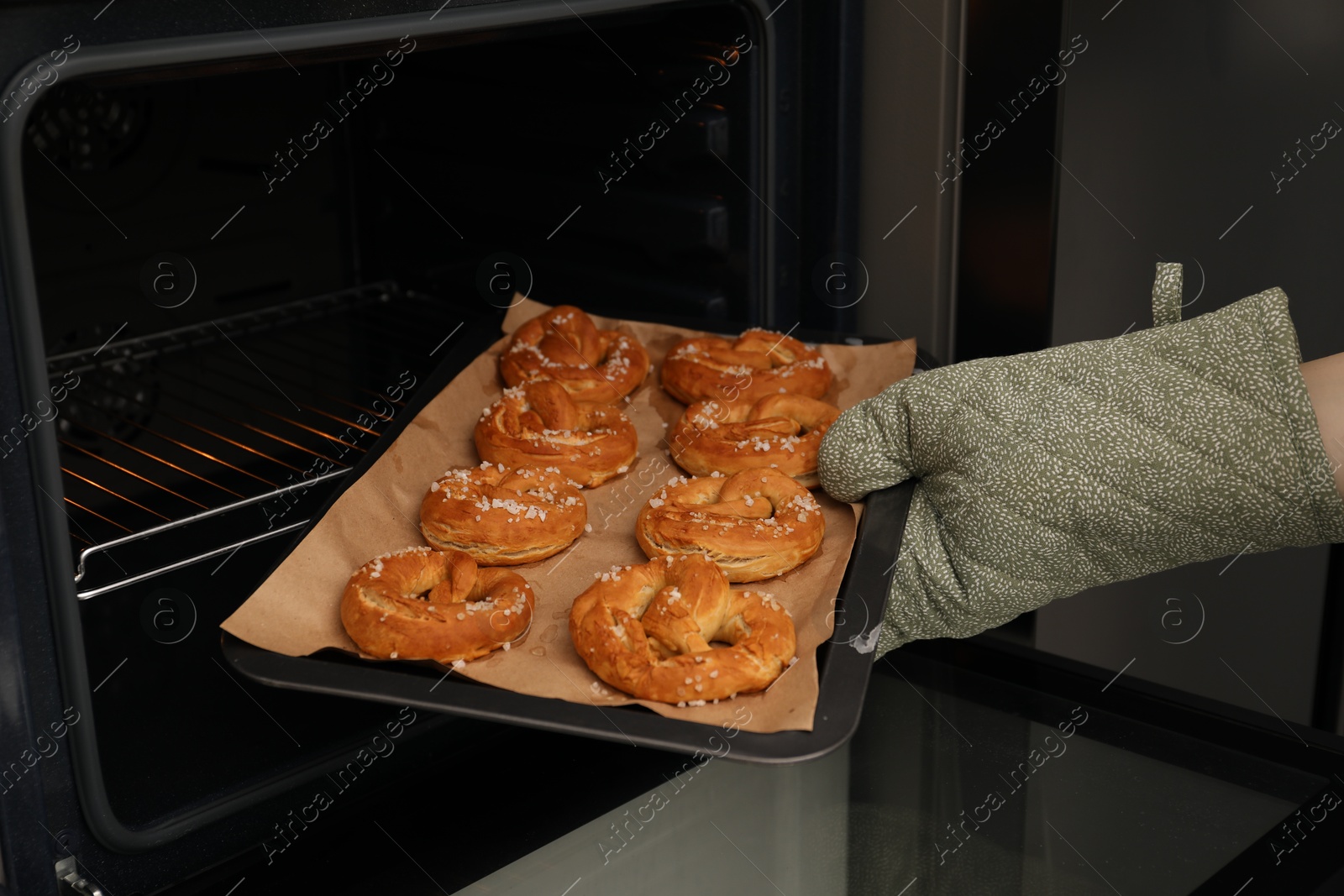 Woman taking baking dish with fresh pretzels out of oven, closeup Photo of Woman taking baking dish with fresh pretzels out of oven, closeup