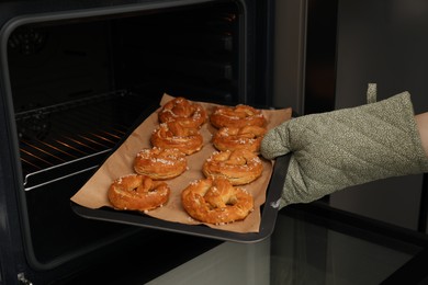 Photo of Woman taking baking dish with fresh pretzels out of oven, closeup