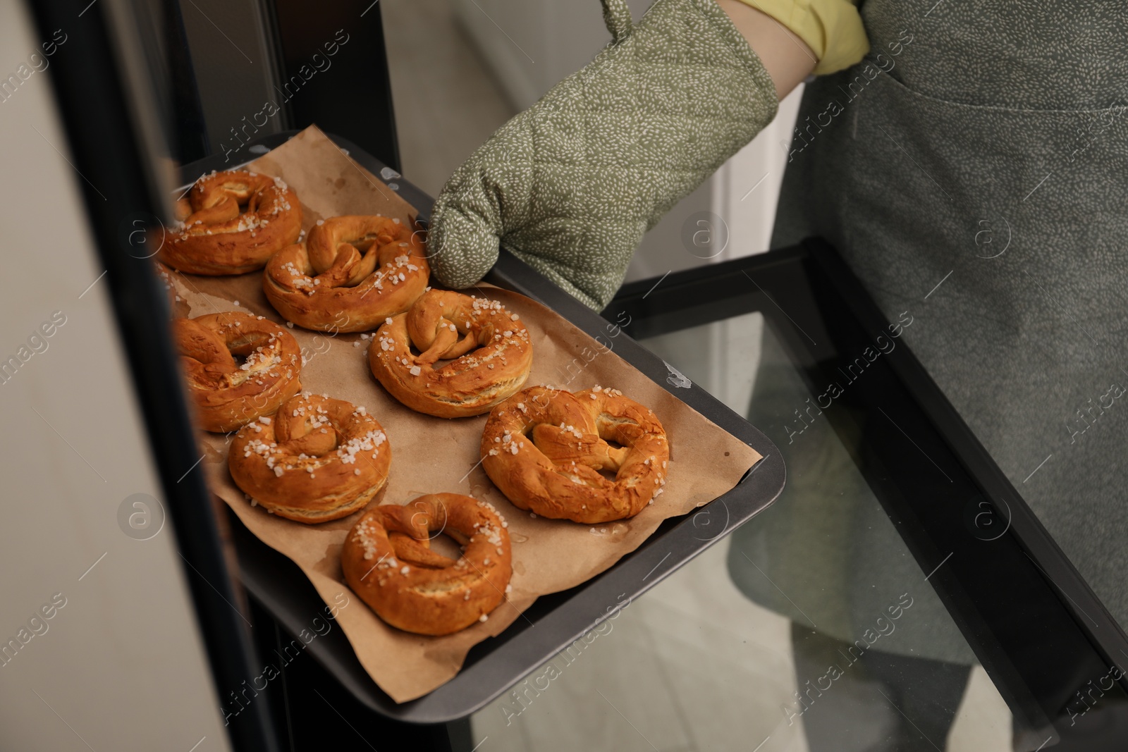 Woman taking baking dish with fresh pretzels out of oven, closeup Photo of Woman taking baking dish with fresh pretzels out of oven, closeup
