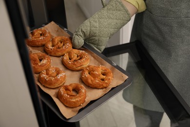 Photo of Woman taking baking dish with fresh pretzels out of oven, closeup