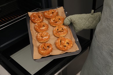 Photo of Woman taking baking dish with fresh pretzels out of oven, closeup