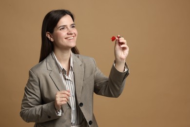 Photo of Targeting. Smiling businesswoman with dart aiming on beige background