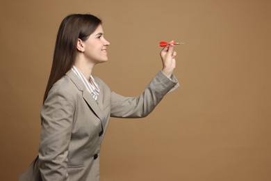 Photo of Targeting. Smiling businesswoman with dart aiming on beige background