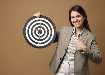 Photo of Targeting. Smiling businesswoman pointing at dart board and arrow on beige background