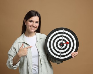 Photo of Targeting. Smiling woman pointing at dart board with arrow on beige background