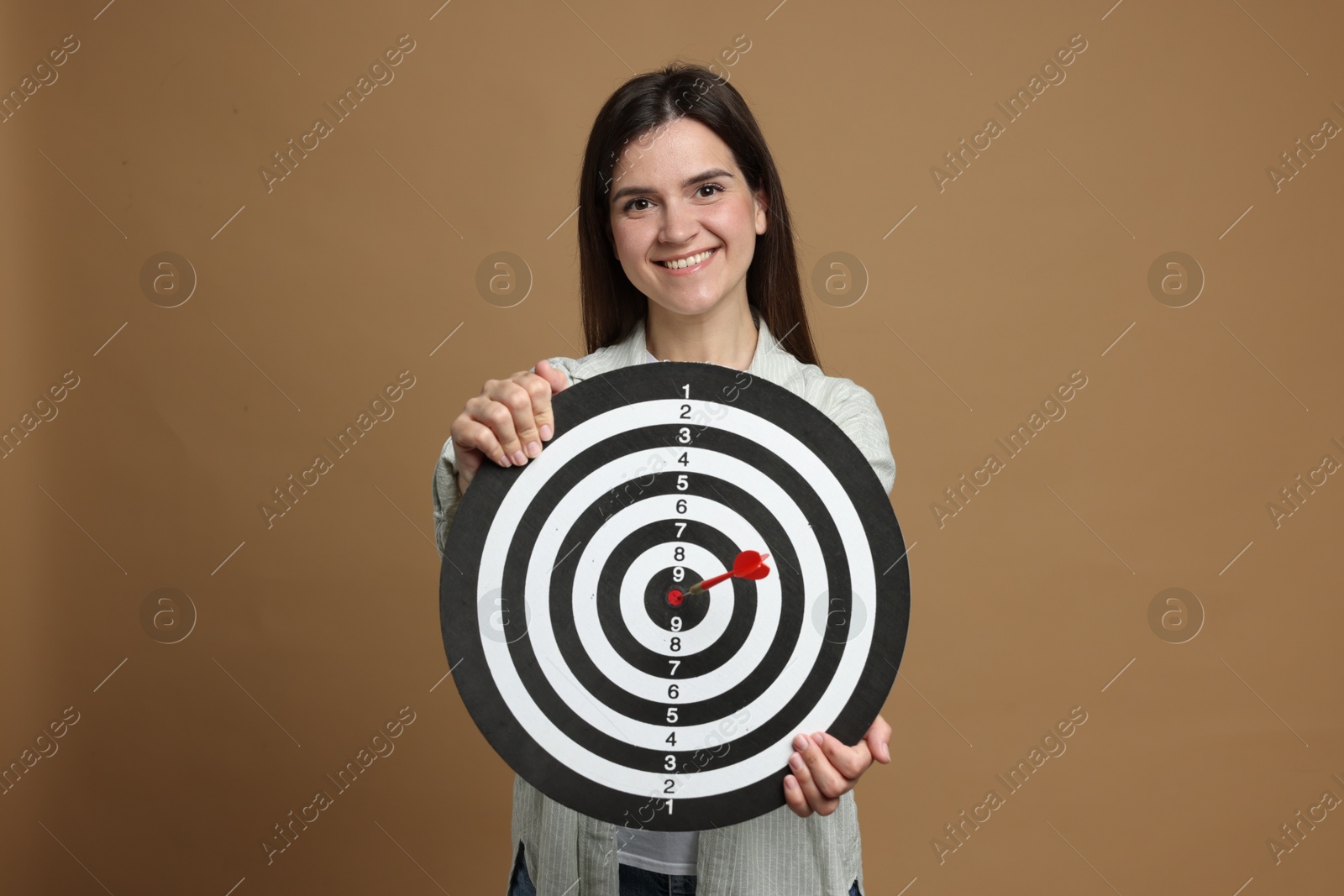 Targeting. Smiling woman with dart board and arrow on beige background Photo of Targeting. Smiling woman with dart board and arrow on beige background