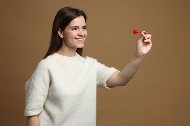 Photo of Targeting. Smiling woman with dart aiming on beige background