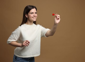 Photo of Targeting. Smiling woman with dart aiming on beige background