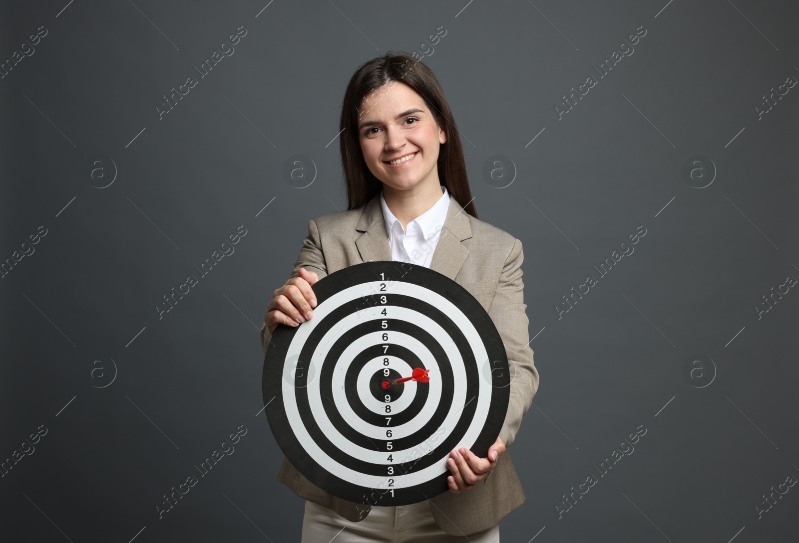 Targeting. Smiling businesswoman with dart board and arrow on grey background Photo of Targeting. Smiling businesswoman with dart board and arrow on grey background