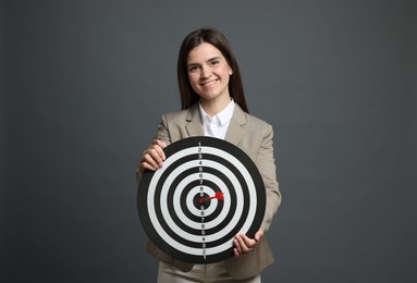 Photo of Targeting. Smiling businesswoman with dart board and arrow on grey background