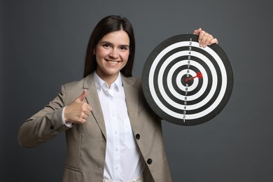 Photo of Targeting. Smiling businesswoman with dart board and arrow showing thumbs up on grey background