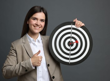 Photo of Targeting. Smiling businesswoman with dart board and arrow showing thumbs up on grey background