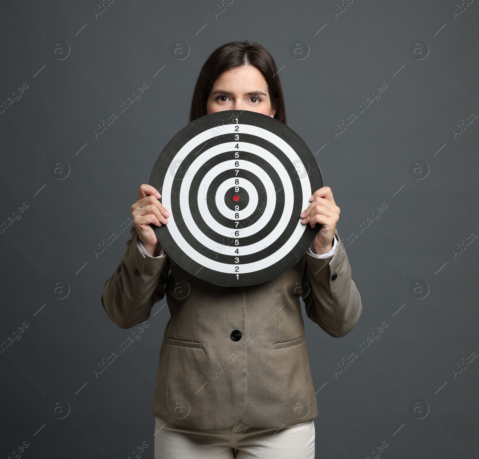 Targeting. Businesswoman with dart board on grey background Photo of Targeting. Businesswoman with dart board on grey background